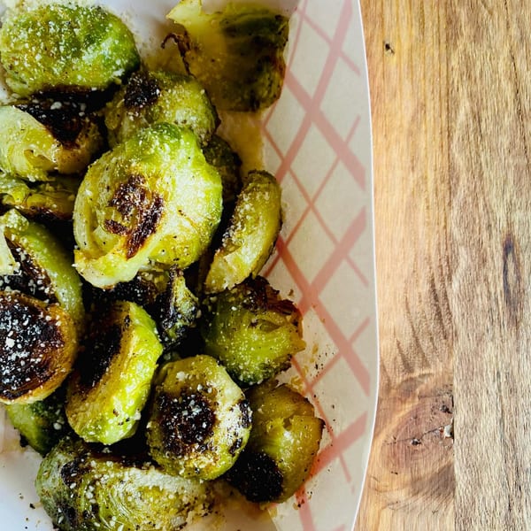 Roasted Brussels sprouts with parmesan cheese and black pepper in a paper tray on a wooden table.