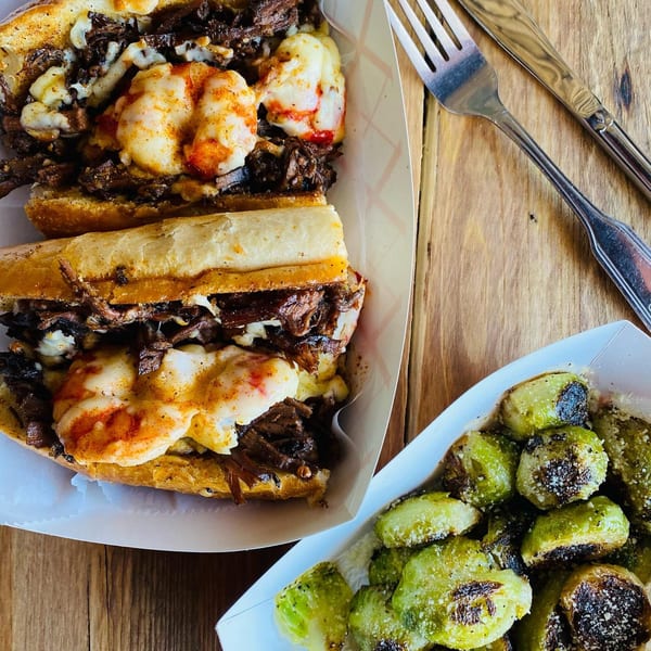 Two Wilson's Secret Sauce BBQ brisket sandwiches with melted cheese and a side of roasted Brussels sprouts.