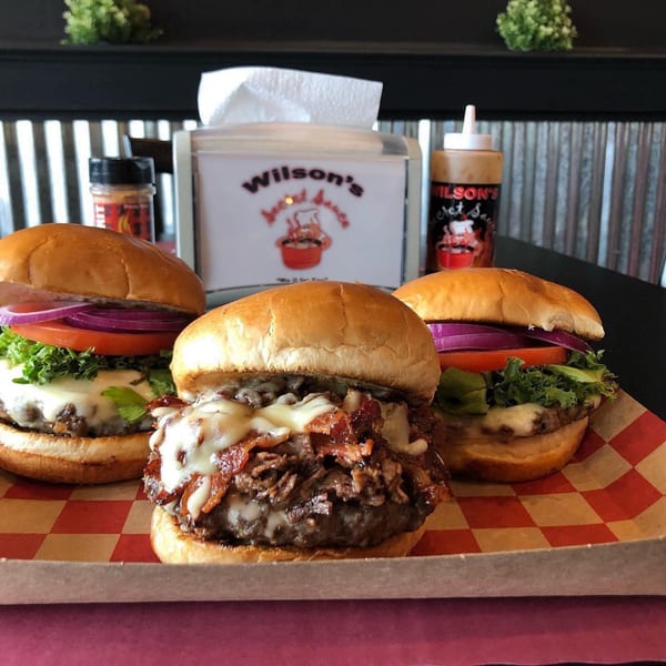 Three Wilson's Secret Sauce burgers on a checkered tray, with a sauce bottle and napkin dispenser.