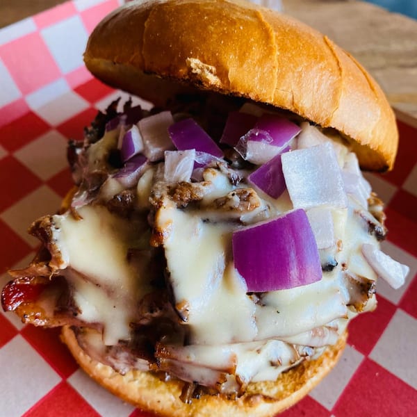 Wilson's Secret Sauce BBQ sandwich with melted cheese and diced red onions on a red and white checkered paper.